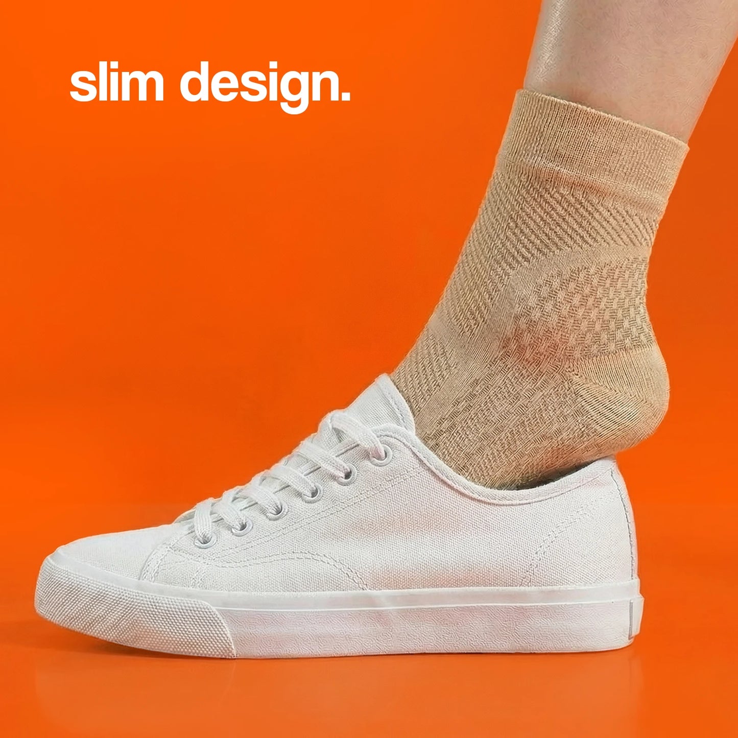 Compression socks in a slim design, worn with a white sneaker against an orange background.