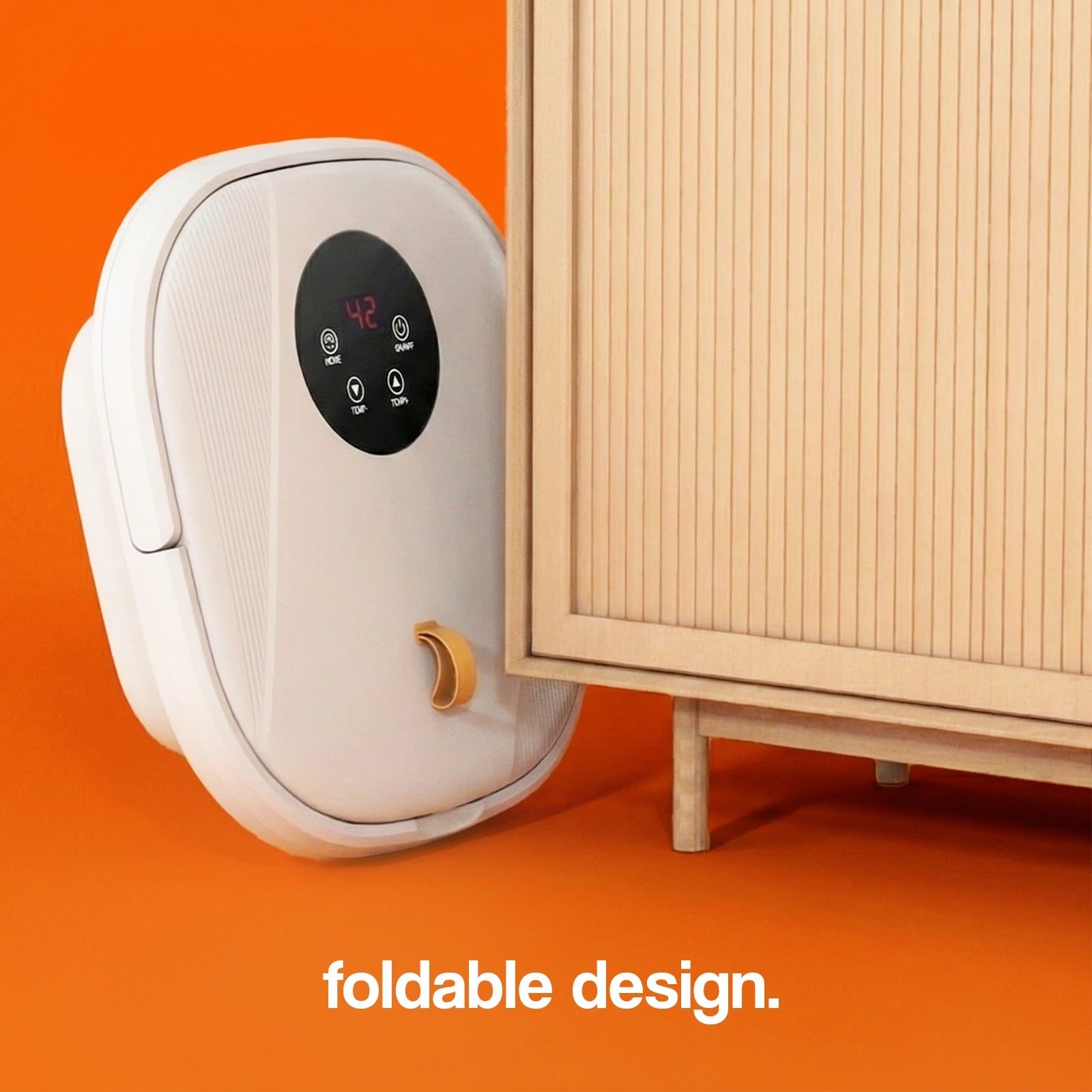 Foldable foot spa massager in white with control panel, positioned next to a wooden cabinet on an orange background.